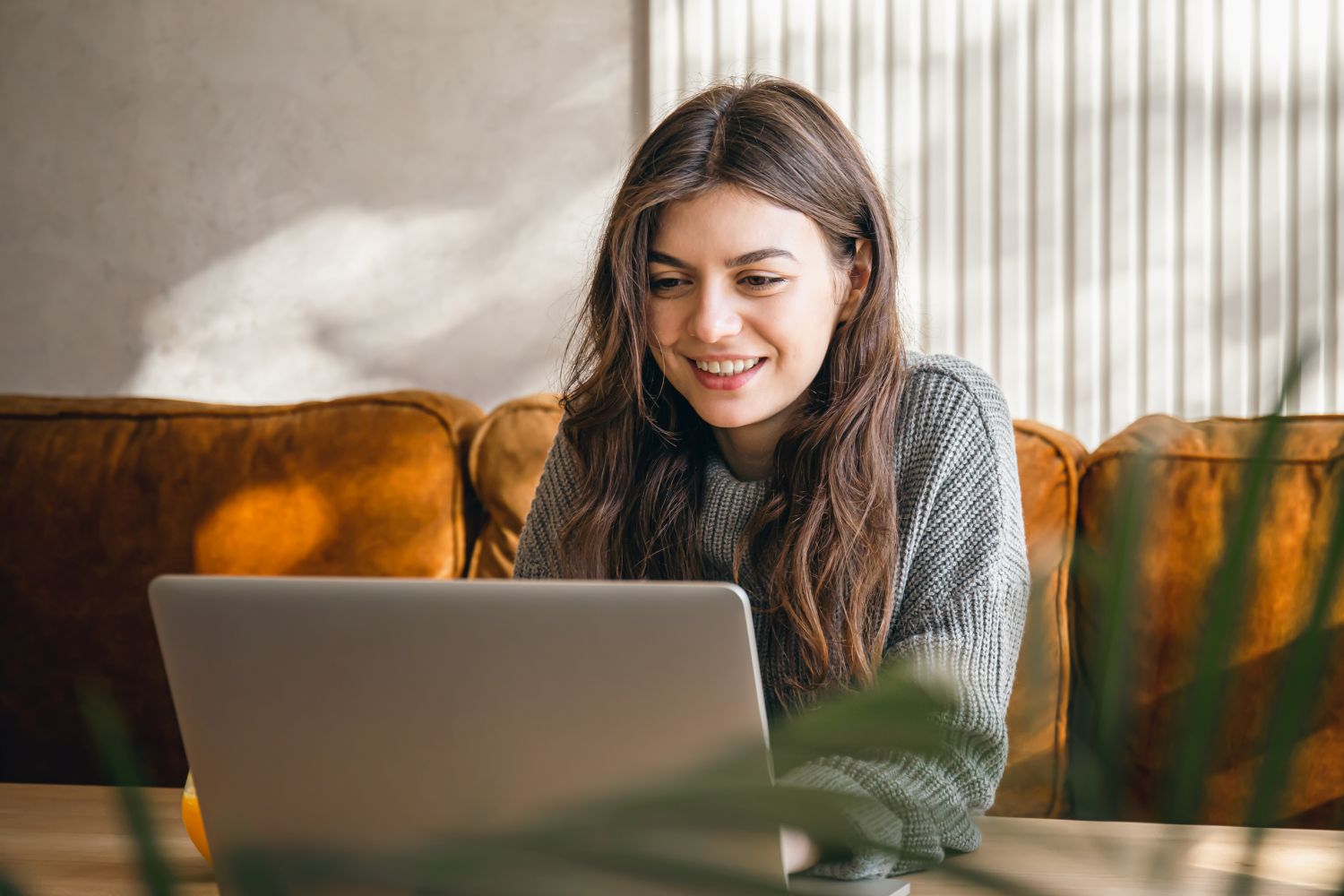 Psicóloga sentada no sofá, sorrindo, mexendo no computador criando um site para psicólogo.